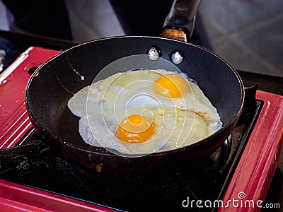 Twin fried egg in pan. Close up top view of the double fried eggs on a frying pan with red picnic gas stove. Stock Photo