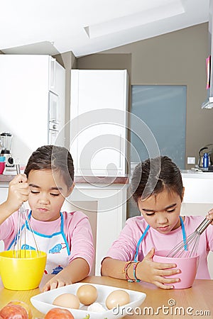 Twin Sisters Beating Eggs in Kitchen Stock Photo