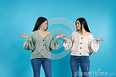 Twin women spread their palms to the sides looking at each other. Emotions for your advertisment on blue background Stock Photo