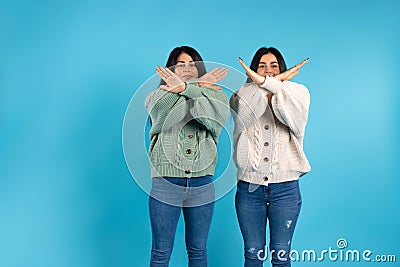 Twins, brunettes in the same clothes on a blue background, crossed their arms, showing stop. Side space. Stock Photo