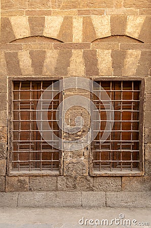 Two adjacent wooden closed windows with iron grid over decorated stone bricks wall, Medieval Cairo, Egypt Stock Photo