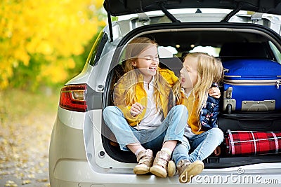 Two adorable girls sitting in a car trunk before going on vacations with their parents. Two kids looking forward for a road trip o Stock Photo