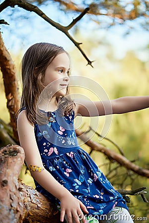 Two girls in summer dresses are climbing a tree in the forest Stock Photo