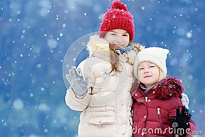 Two adorable little girls having fun together in beautiful winter park. Beautiful sisters playing in a snow. Stock Photo