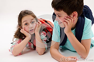 Smart school kids, first grader little child girl and preteen schoolboy, lying on belly, smiling over white background Stock Photo