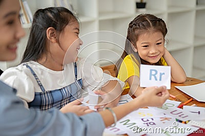 Two adorable young Asian girls are enjoying studying English alphabet flashcards with a teacher Stock Photo