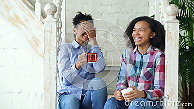 Two african american curly girls sistres sitting on stairs have fun laughing and chatting together at home Stock Photo