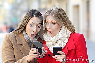Two amazed women finding content on phones Stock Photo