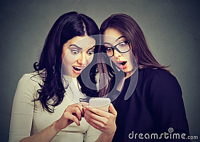 Two amazed women roommates watching offers on line on a smart phone. Stock Photo