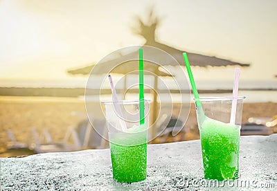 Two apple green drift-ice with straw on the beach. In the background is blue sky, palms, sea nd sandy beach. This is situated in Stock Photo