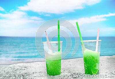 Two apple green drift-ice with straw on the beach. In the background is blue sky, palms, sea nd sandy beach. This is situated in Stock Photo