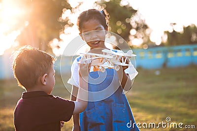 Two asian child girl and boy playing with toy wooden airplane in the park together at sunset time Stock Photo