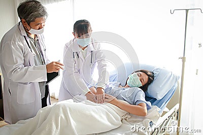 Two Asian doctors examined the abdominal pain of a woman lying in a hospital bed. Stock Photo