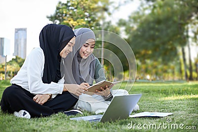 Two Asian Islamic female students sitting in the garden with their laptops while doing their homework Stock Photo