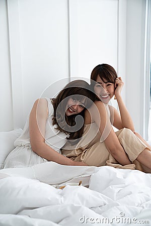 Two asian women smile and laying on bed holding gold stripe ceramic cup / bedroom concept / copy space Stock Photo