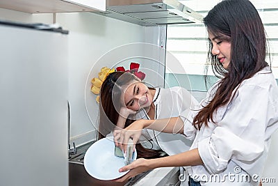 Two Asian women washing dishes together in kitchen. People and Lifestyles concept. LGBT pride and Lesbians theme Stock Photo