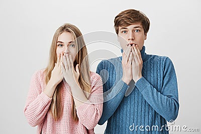 Two astonished horrified young students in stylish sweaters staring at camera in full disbelief, keeping mouths opened Stock Photo