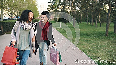 Two attractive mixed race women dancing and have fun while walking down the park with shopping bags. Happy young friends Stock Photo