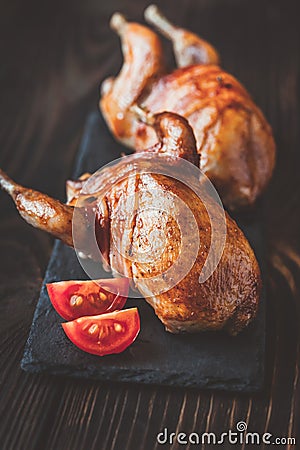 Two baked quails wrapped in bacon on the black stone board Stock Photo