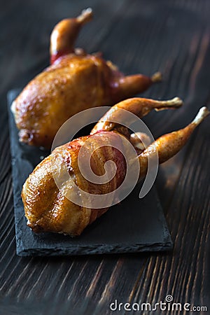 Two baked quails wrapped in bacon on the black stone board Stock Photo