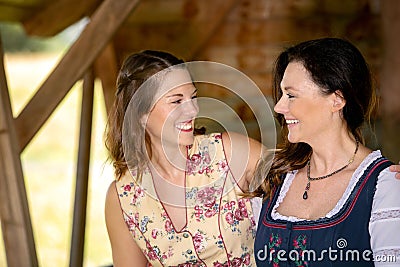 Two bavarian women in dirndl sitting by a wooden hut Stock Photo