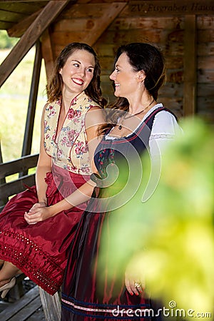 Two bavarian women in dirndl standing by a wooden hut Stock Photo