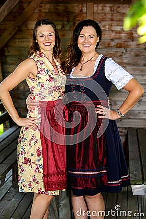 Two bavarian women in dirndl standing by a wooden hut Stock Photo