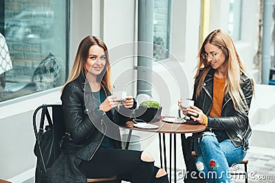 Two beautiful attractive stylish women are sitting outdoor in cafe drinking coffe and tea talking and enjoying great day. Stock Photo