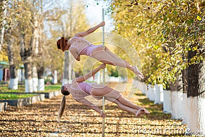 Two beautiful gymnasts do pair tricks on a portable platform in a beautiful autumn park. Two friends in the same body Stock Photo