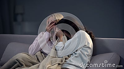 Two beautiful scared girls watching horror movie at night, frightening episode Stock Photo