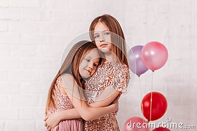 Two beautiful school-age girls in dress in a white room cuddle Stock Photo