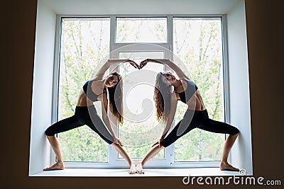 Two beautiful women doing yoga asana showing heart symbol on win Stock Photo