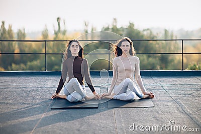 Two beautiful women perform meditative pose on the roof Stock Photo