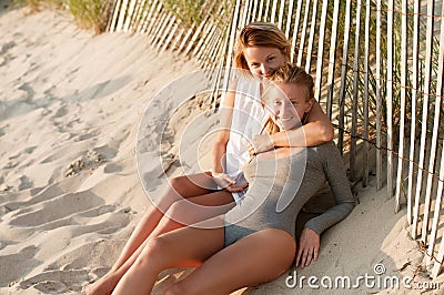 Two beautiful young girls sitting on the beach at the sunset Stock Photo