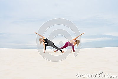 Two beautiful young women performing yoga pose parivrita parshvakonasana Stock Photo