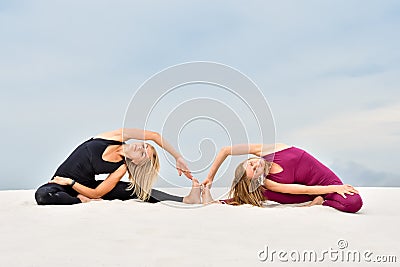 Two beautiful young women performing yoga pose Parivritta Janu Sirshasana Stock Photo