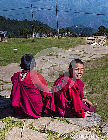 Two cute Bhutanese novice young monks sit on footstep , one turns his head and smiles Editorial Stock Photo