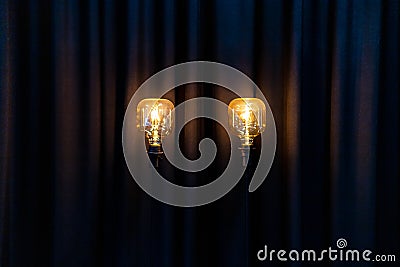 Two big decorative bulbs with golden warm light on long black pole in front of long curtain Stock Photo