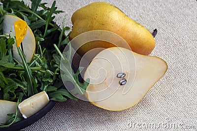 Two big sweet pears near the black plate. Easy tasty summer salad with pear, arugula, brie cheese, pine nuts, honey sauce. The Stock Photo