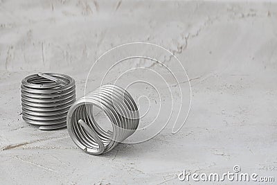 Two big wire thread inserts, grey color, free running on grey cement background. Stainless Steel. Horizontal with copy space for Stock Photo