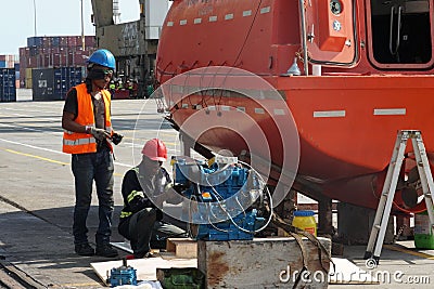 Two black mechanics or technicians repair engine of orange lifeboat. Editorial Stock Photo