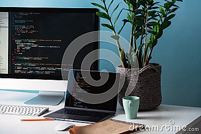 Two black screens, laptop and monitor, filled with program code lines on desk Stock Photo