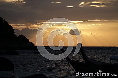 Two boat and rock shadow in front of Golden rays of dawn light shining through idyllic beach and ocean, backgrounds Stock Photo