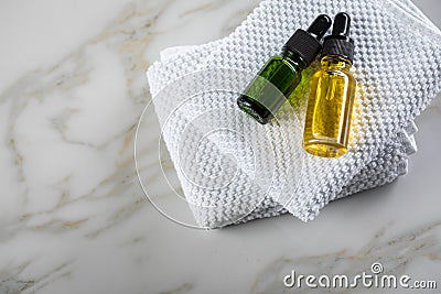 Two bottles of green natural serum and yellow organic beauty face oil for cosmetic anti age treatment skin care on towels and Stock Photo