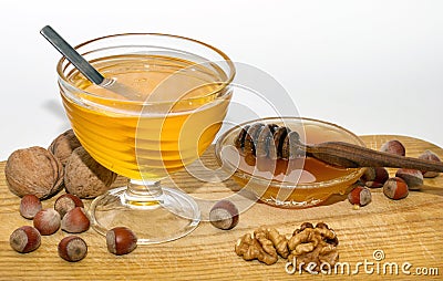 Two bowls with dark and light honey, hazelnuts, walnuts on wooden table with white background Stock Photo
