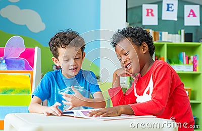 Two boy kid sit on table and reading tale book in preschool lib Stock Photo