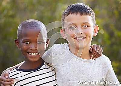 Two boys, arms around each other smiling to camera outdoors Stock Photo