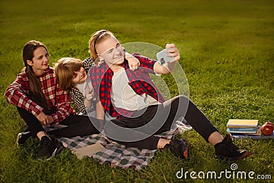 two boys brothers with girl sister make selfie on phone on green grass in summer picnic ourdoors Stock Photo