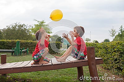 Two boys, brothers, playing with yellow balloon in the park Stock Photo