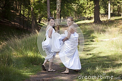 Two brides walk on forest path with skirts in their arms Stock Photo